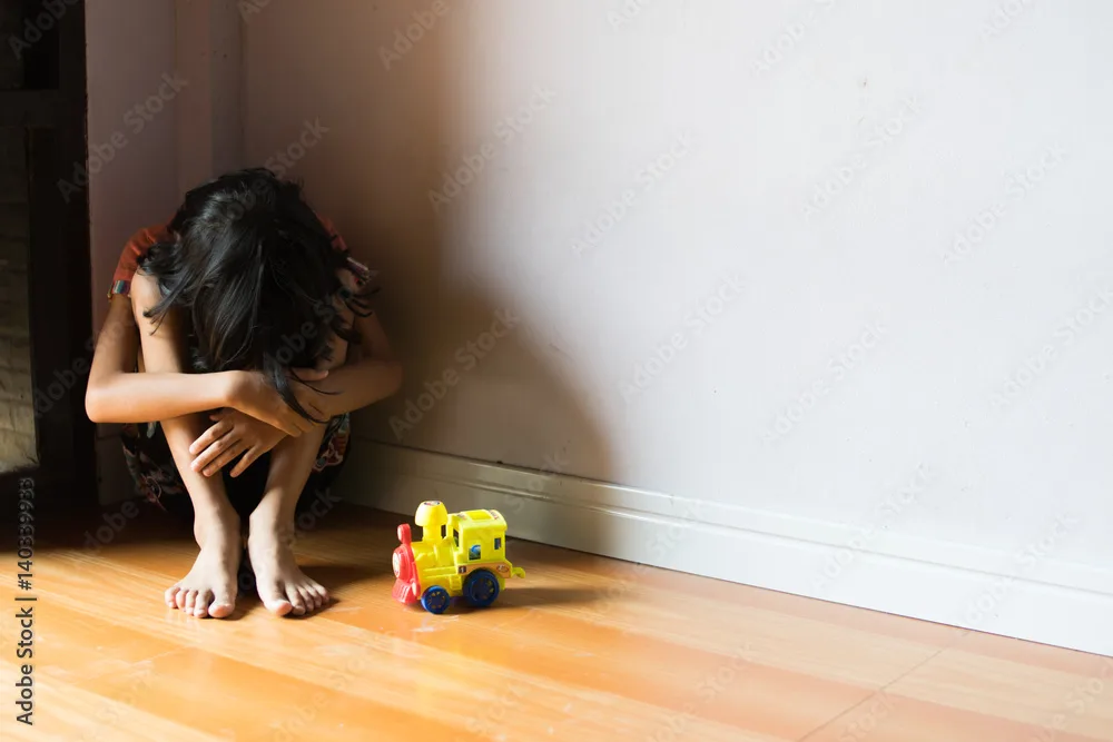 un niño pequeño, sentado en un rincón solitario.